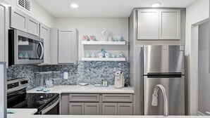 Eine moderne Küche mit Edelstahlgeräten, grauen Schränken und einer blauen Mosaik-Spritzwand.