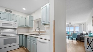 Eine moderne Küche mit weißen Geräten, hellblauen Schränken und Blick in einen Wohnbereich mit einem Balkon.