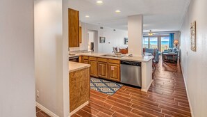 A modern kitchen with wooden cabinets, a dishwasher, and a view to the living area. - La Mirage Condo 329 Beachfront Condominiums Resort with Private Boardwalk to Beach (Port Aransas)