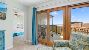 A room with a bed, a chair, a sofa, and a balcony with a view of the beach.