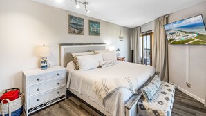 A bedroom with a large bed, bedside tables, a TV, and artwork on the wall. - La Mirage Condo 240 Beachfront Resort Condominiums with Private Boardwalk to Beach (Port Aransas)