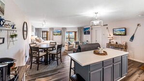 A modern kitchen with a central island, dining area with chairs, and a living space with a sofa and a TV. - La Mirage Condo 240 Beachfront Resort Condominiums with Private Boardwalk to Beach (Port Aransas)