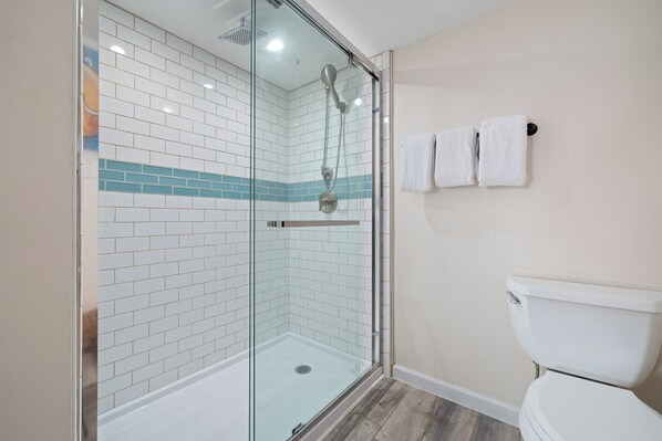 Un baño con ducha envuelta en cristal, inodoro blanco y paredes con azulejos.