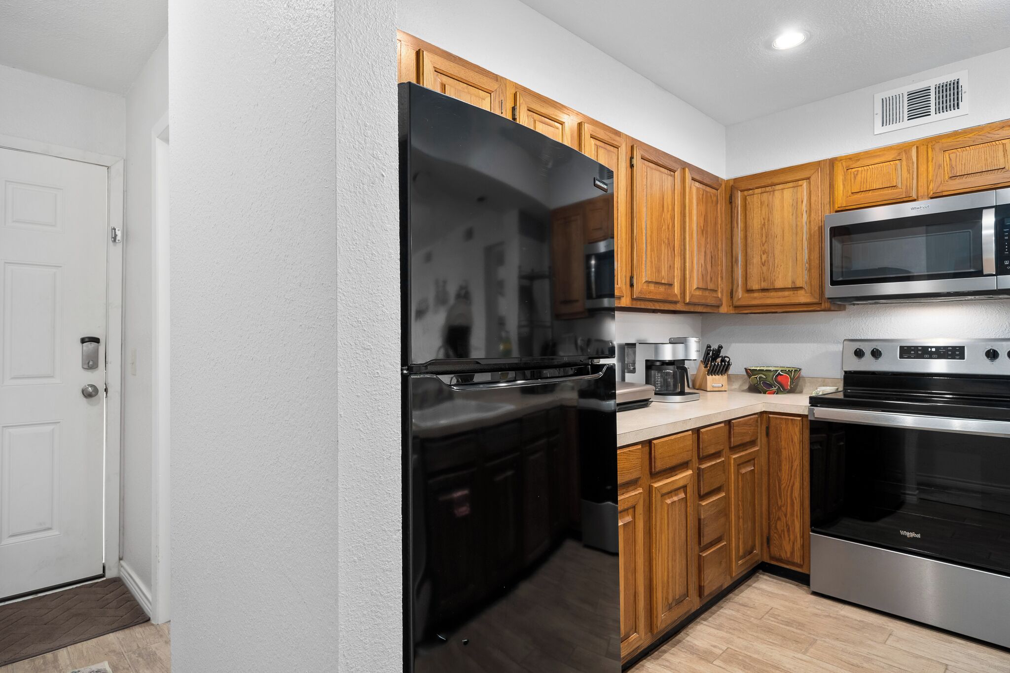 A modern kitchen with wooden cabinets, a stainless steel refrigerator, a microwave, and an oven.