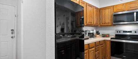 A modern kitchen with wooden cabinets, a stainless steel refrigerator, a microwave, and an oven.