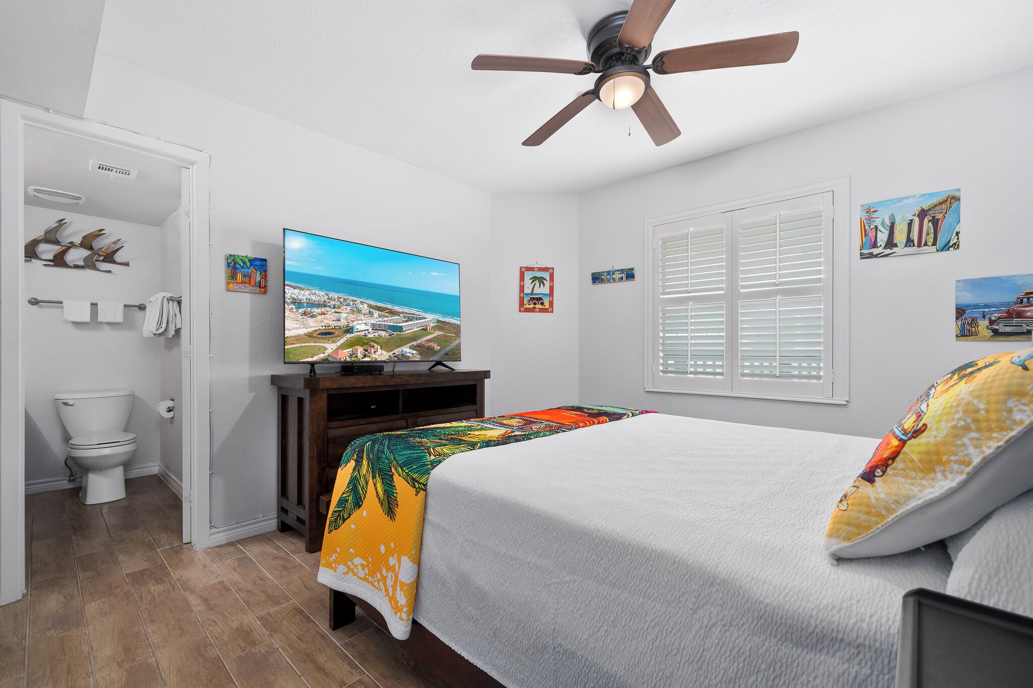 Una camera da letto con un letto, una ventola a soffitto, una televisione e una finestra con persiane.
