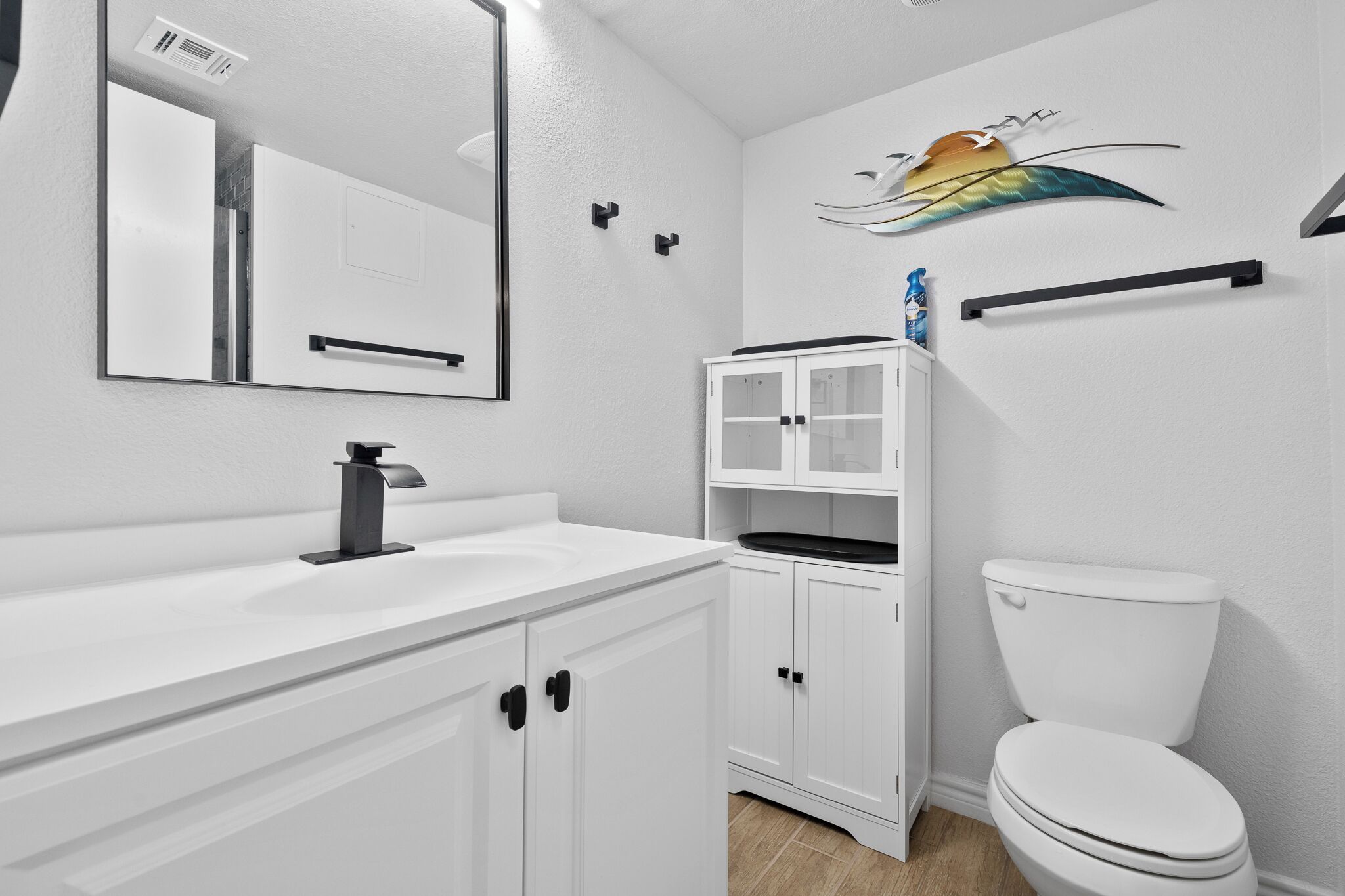 A bathroom with a white sink, mirror, cabinet, and toilet.