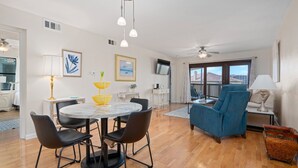 A spacious living area with a dining table, chairs, a blue armchair, and a television.