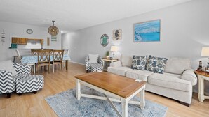 A living room with a wooden coffee table, a beige sofa, and patterned ottomans. - La Mirage Condo 103 Beachfront Condo Resort with Private BoardWalk Access (Port Aransas)