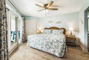 Een slaapkamer met een bed, twee nachtkastjes met lampen, een plafondventilator en een schuifdeur naar een buitenruimte.