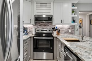 A modern kitchen with stainless steel appliances, a marble countertop, and white cabinetry.