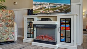 Ein Wohnzimmer mit Kamin, einem darüber angebrachten Fernseher und Blick auf die Küste.
