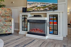A living room with a fireplace, a television mounted above it, and a view of a coastal area. - La Mirage Condo 130 Beachfront Condominium Resort with Private Beach Boardwalk Access (Port Aransas)
