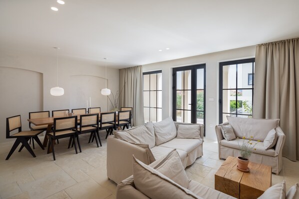 Un salon spacieux comprenant un grand canapé, une table à manger avec des chaises et une table basse agrémentée d’une plante.