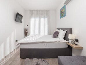 Un dormitorio moderno con una cama grande, una mesita de noche con lámpara y un televisor montado en la pared.