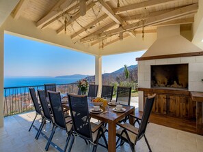 Un patio con mesa y sillas de madera, una chimenea y vista al mar.