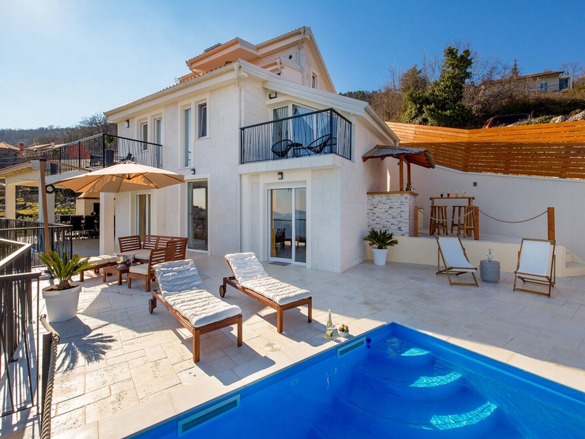 A modern two-story house with a swimming pool, outdoor seating, and a balcony.