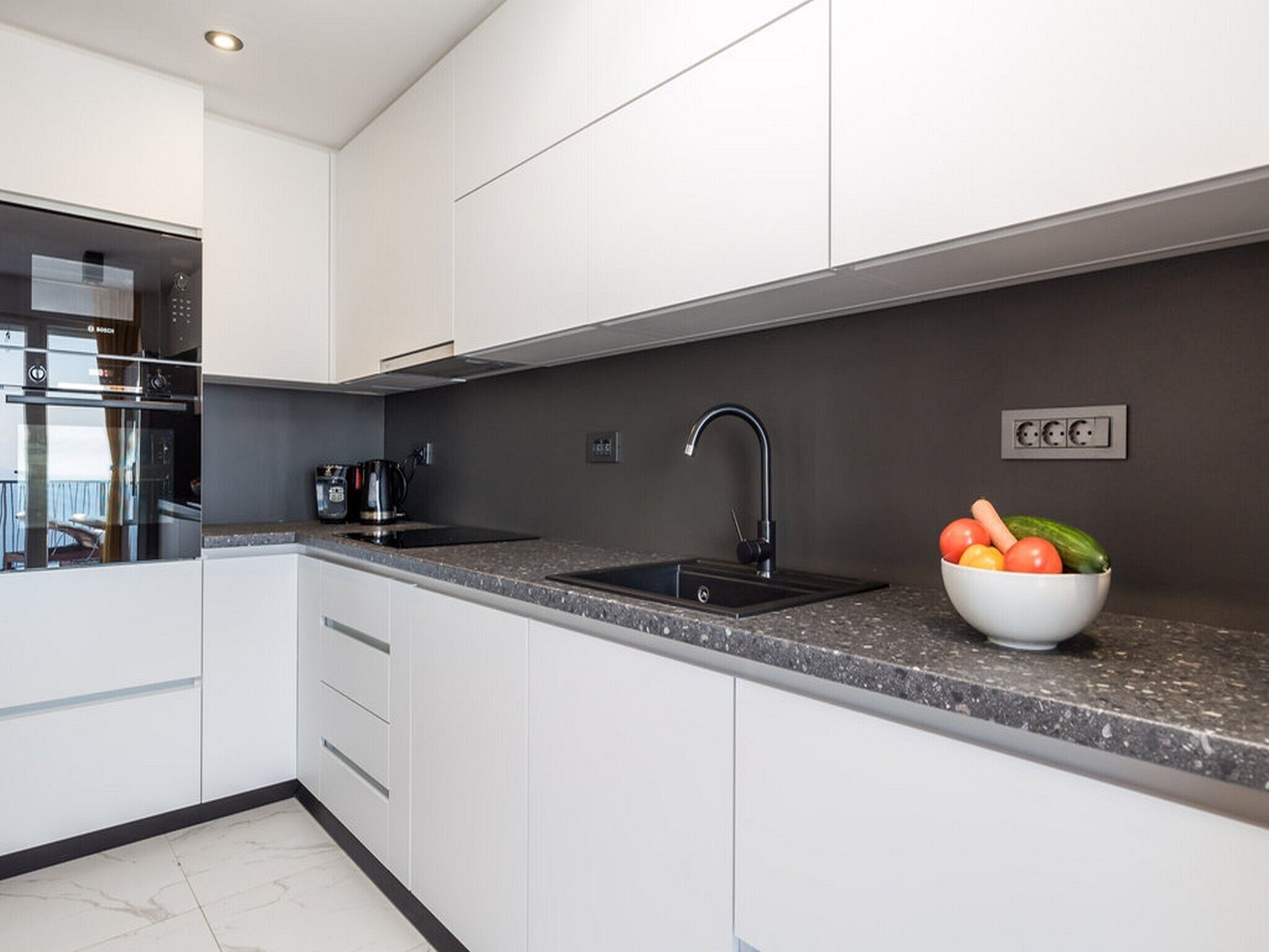 A modern kitchen with white cabinets, a black sink, and a granite countertop.