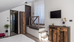 Quarto moderno com cama grande, escada de madeira, TV e mesa de apoio.