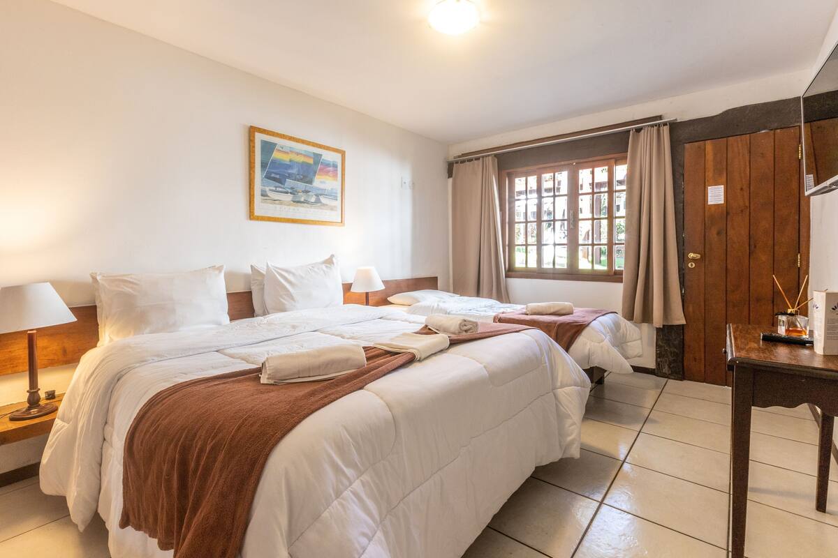 Une chambre d’hôtel avec un grand lit, une table de chevet avec une lampe, une fenêtre avec des rideaux et une armoire en bois.