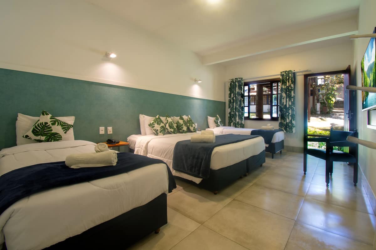 Une chambre d’hôtel avec trois lits, un bureau et une vue sur l’extérieur.
