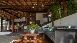 Un vaste espace intérieur doté d’un plafond en bois, d’un sol en pierre et d’un coin salon agrémenté de coussins à motifs.