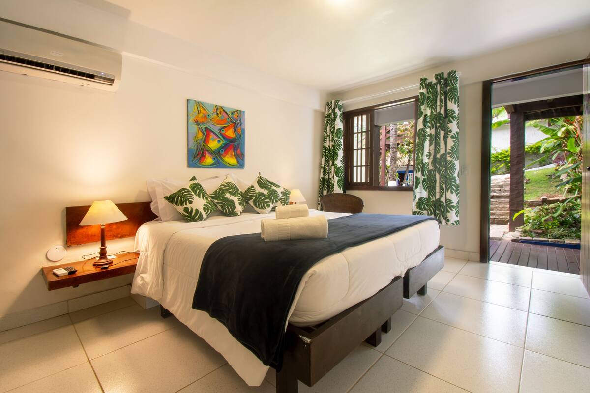 Une chambre à coucher avec un lit, une table de chevet, une lampe, un tableau et une fenêtre avec des rideaux.