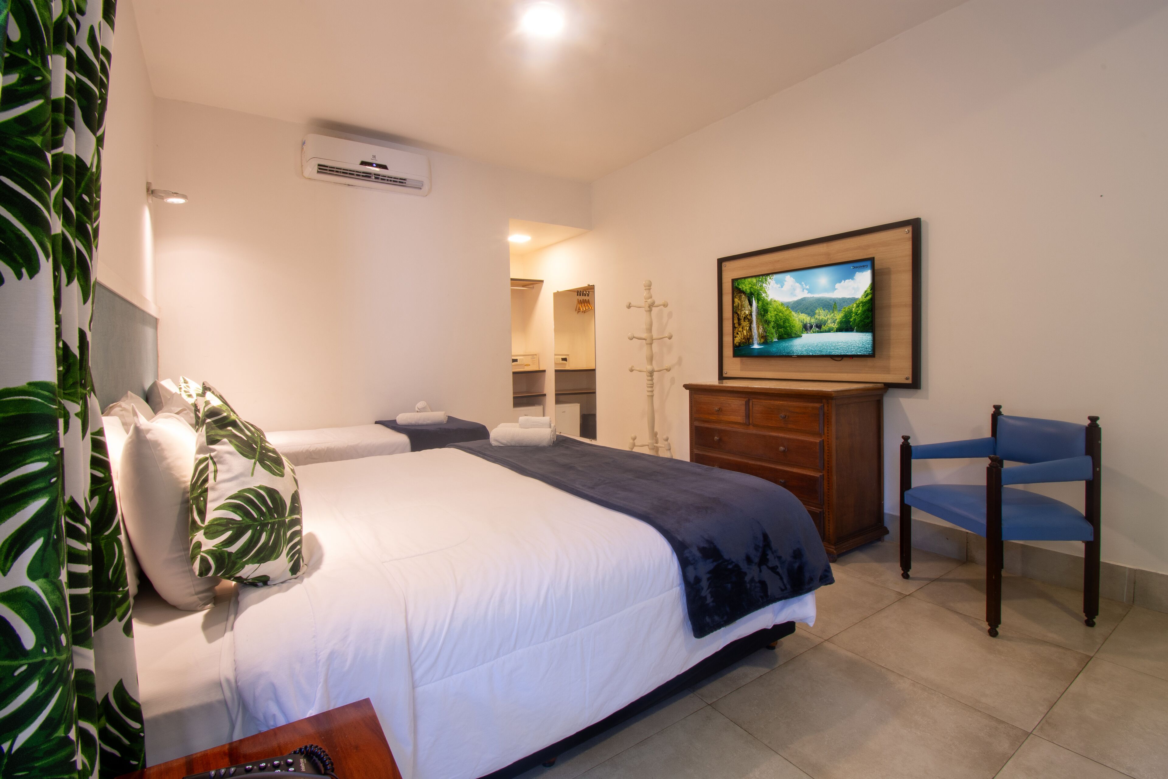 A hotel room with a bed, a television, a chair, a dresser, and a mirror.