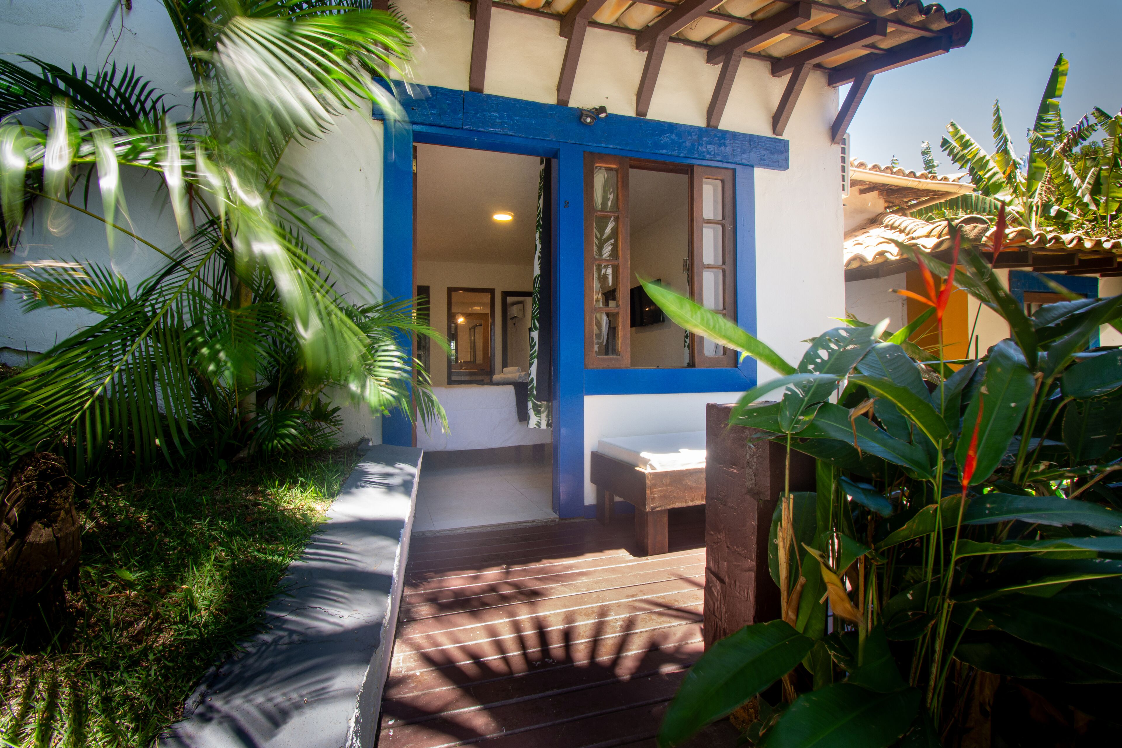 A wooden deck leading to a building with a blue and white facade, surrounded by lush greenery.