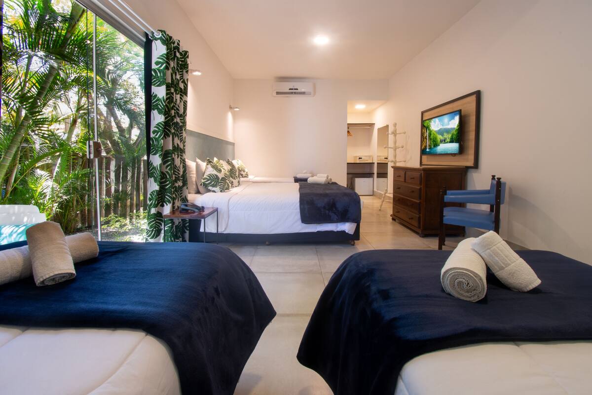 Une chambre d’hôtel avec deux lits, une télévision, un bureau et une vue sur la végétation tropicale.