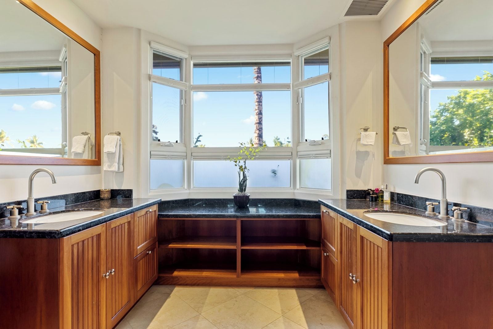 A bathroom with two sinks, wooden cabinets, a large window, and a potted plant.