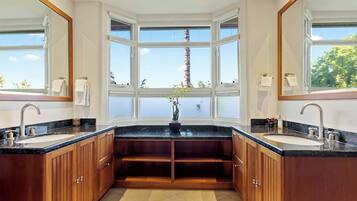 A bathroom with two sinks, wooden cabinets, a large window, and a potted plant.