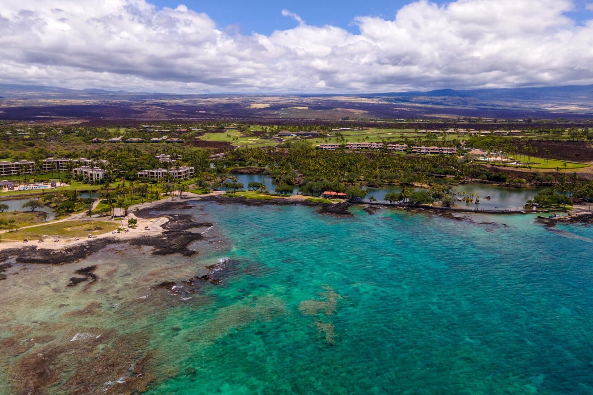 An aerial view of a coastal resort with clear turquoise waters, a golf course, and multiple buildings.