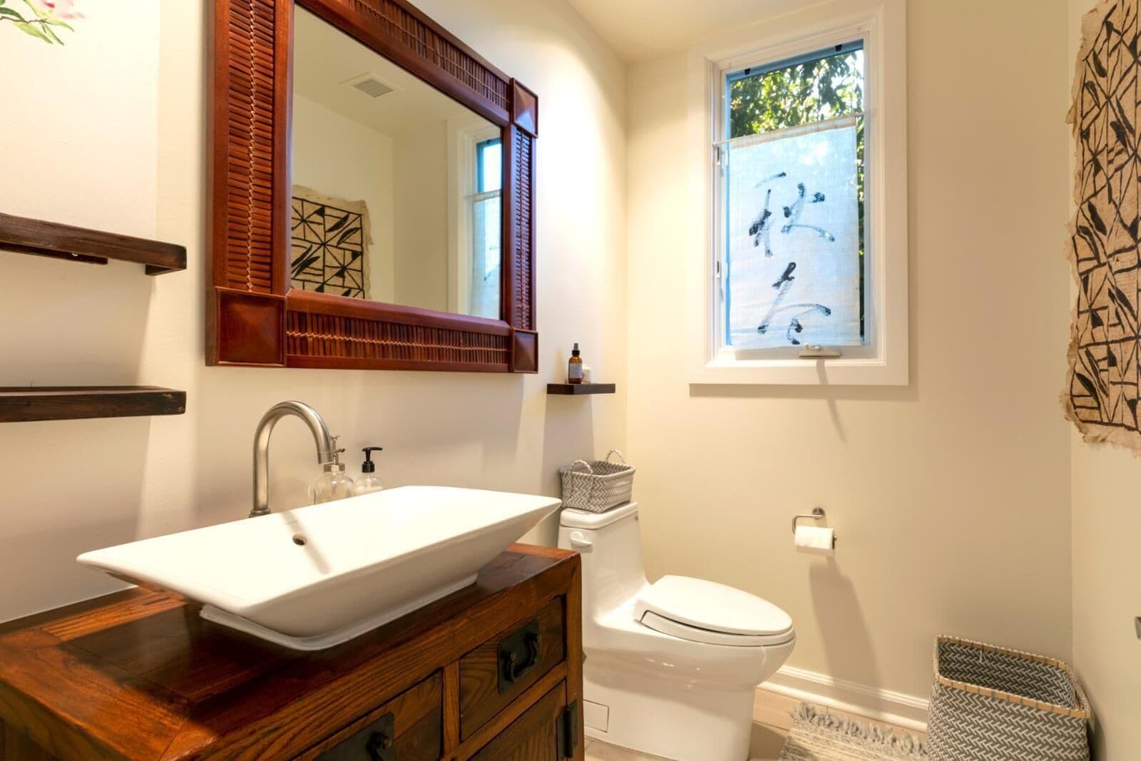 Un baño con un lavabo de pedestal grande, un mueble de tocador de madera, un inodoro y una ventana con vistas a árboles.