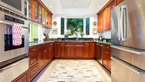 Een moderne keuken met houten kastjes, roestvrijstalen apparatuur en een groot raam met uitzicht op groen.