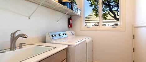 A compact laundry room with a washing machine, a sink, and a window with a view of trees.