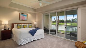 A bedroom with a large bed, a ceiling fan, a sliding glass door leading to a balcony with a view of a golf course.