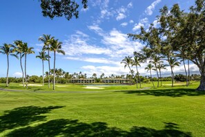 A golf course with palm trees, a clubhouse, and a clear blue sky.