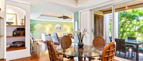 A dining area with a glass table, wooden chairs, and a view of the outdoors.