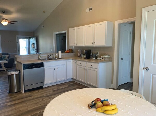 A modern kitchen with white cabinets, a dishwasher, and a dining area with a round table.