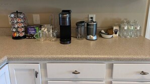 En köksbänk med diverse utrustning för att göra kaffe, inklusive en kaffebryggare, en kaffekvarn och ett ställ för kaffekapslar.