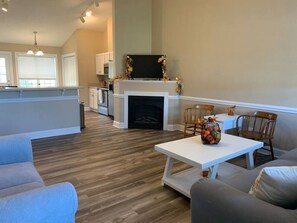 A modern living room with a fireplace, a dining area, and a kitchen in the background.
