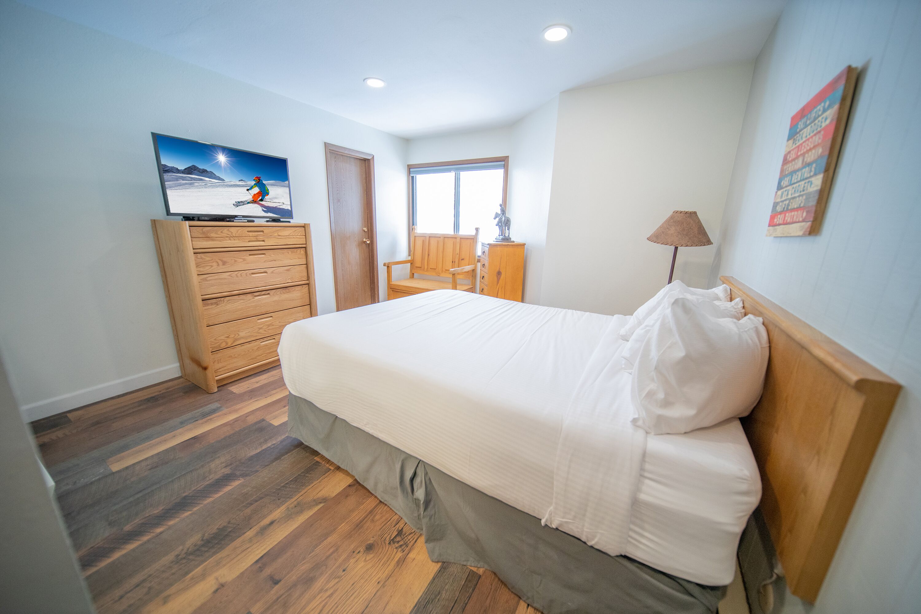 A bedroom with a bed, wooden dresser, and a television displaying a skier.