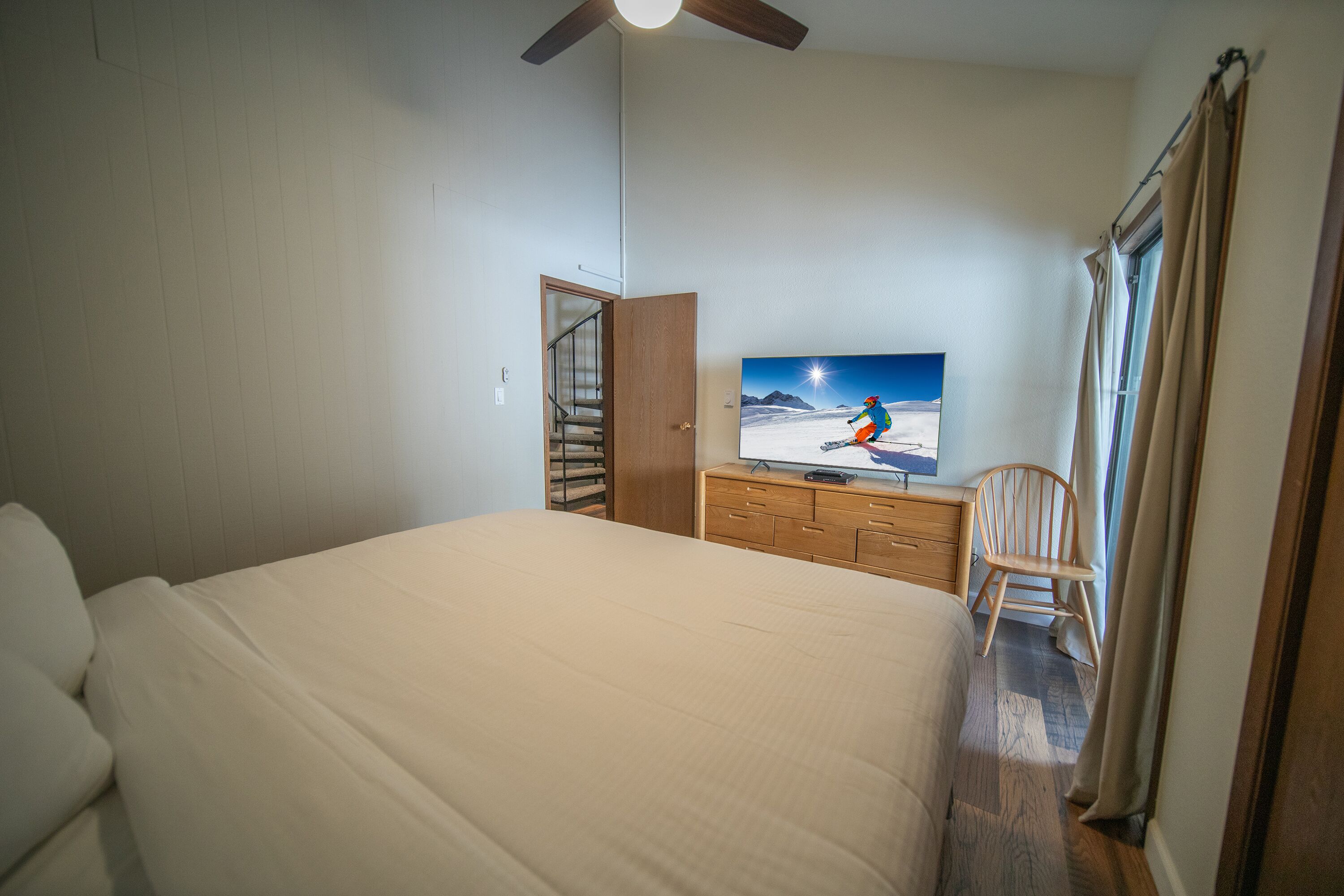 A bedroom with a large bed, a television on a dresser, a chair, and a staircase leading to another room.