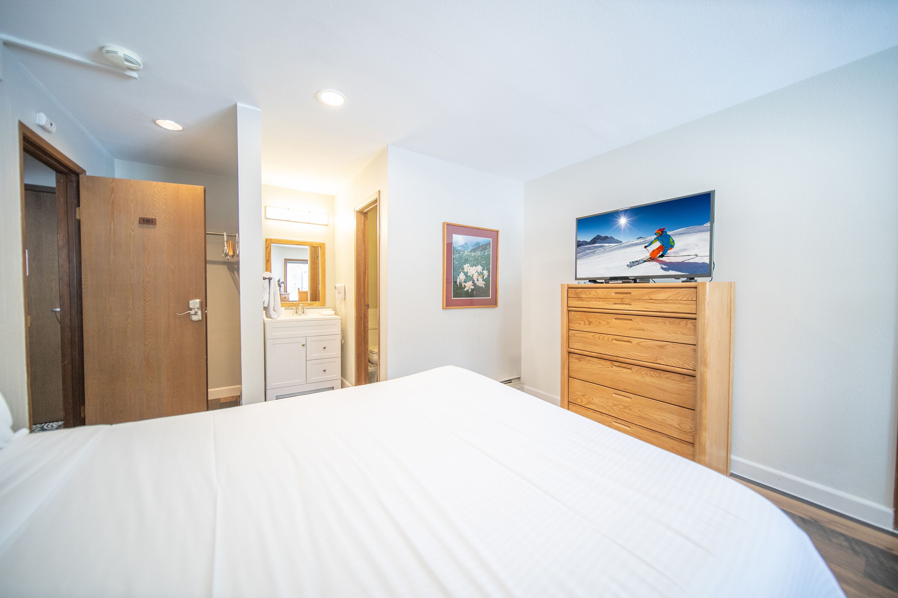 Een hotelkamer met een groot bed, een houten garderobe, een wandtelevisie en een badkamer met spiegel en wastafel.