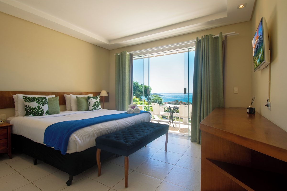 Habitación de hotel con una cama, un banco, un escritorio y vista al océano.