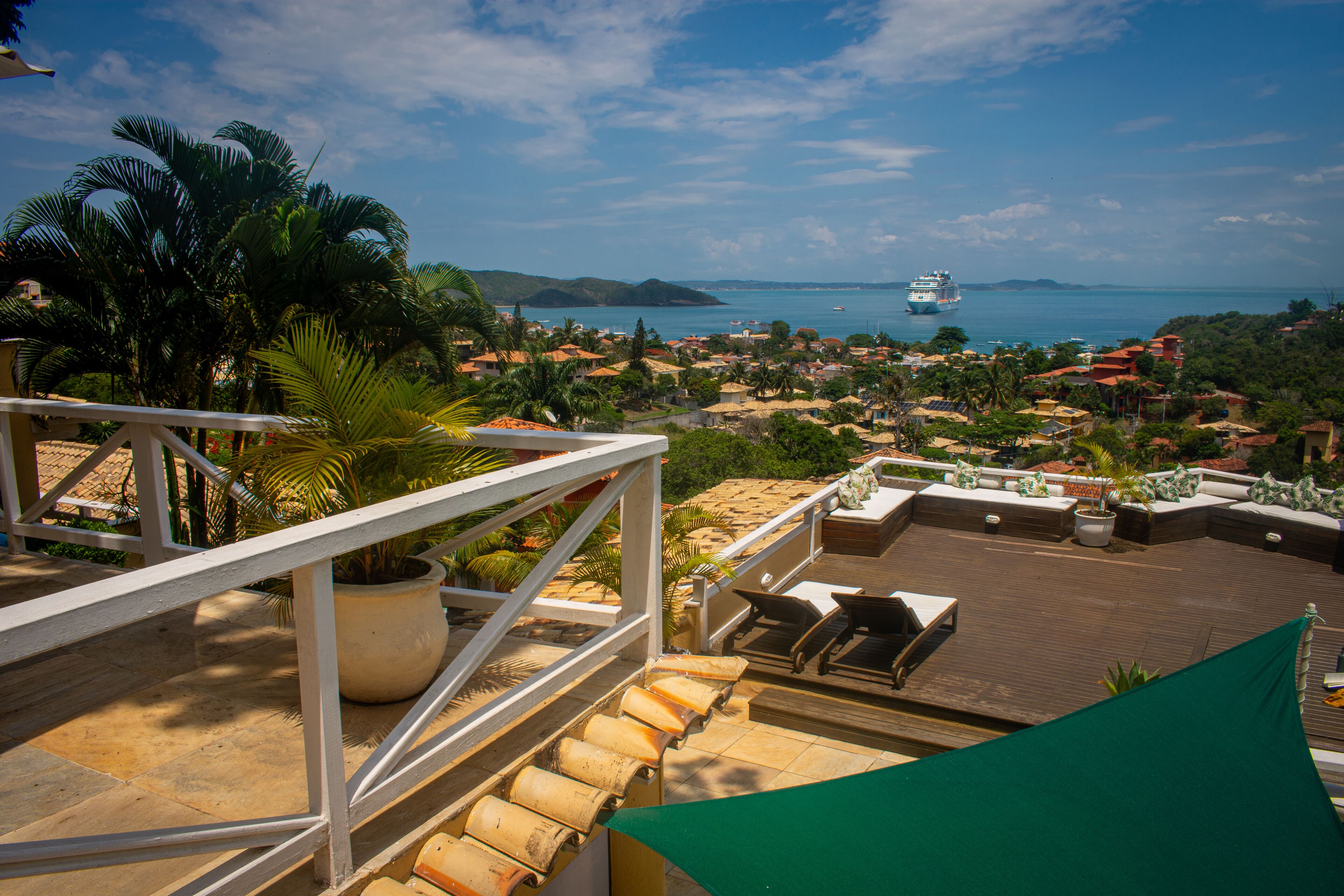 A rooftop terrace with a view of the sea, palm trees, and a cruise ship in the distance.