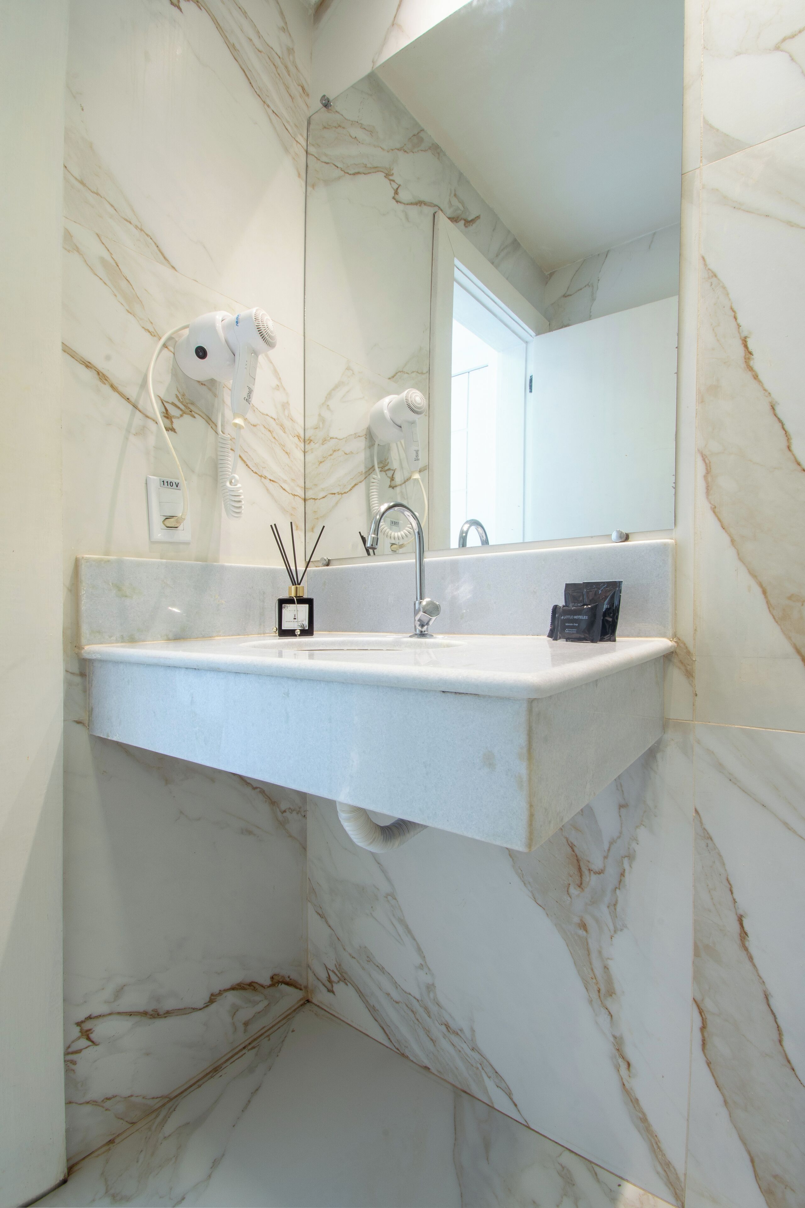 A bathroom with a marble sink, a mirror, and a hairdryer mounted on the wall.