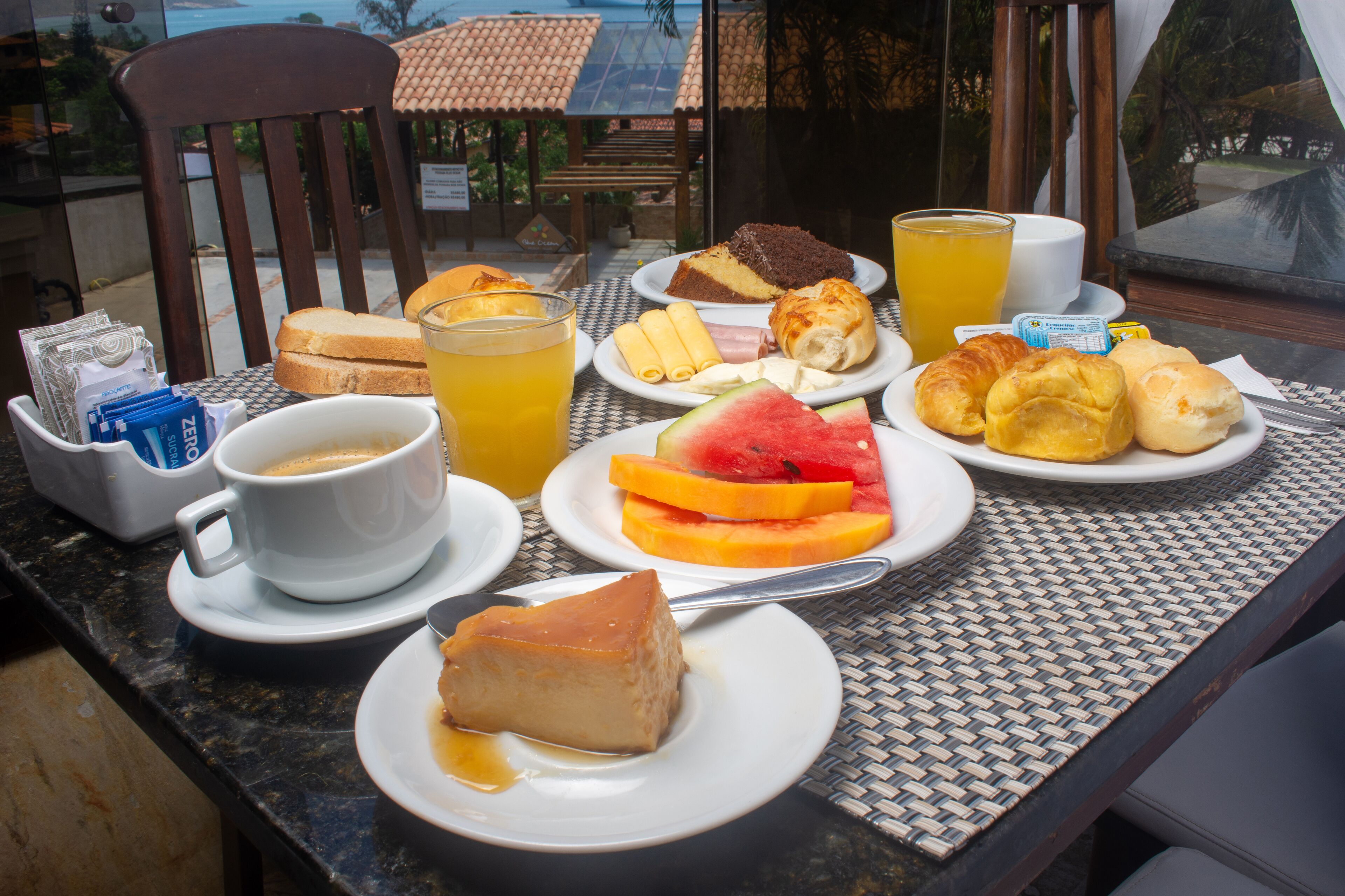 A breakfast table with various food items, a cup of coffee, and a view of the outdoors.