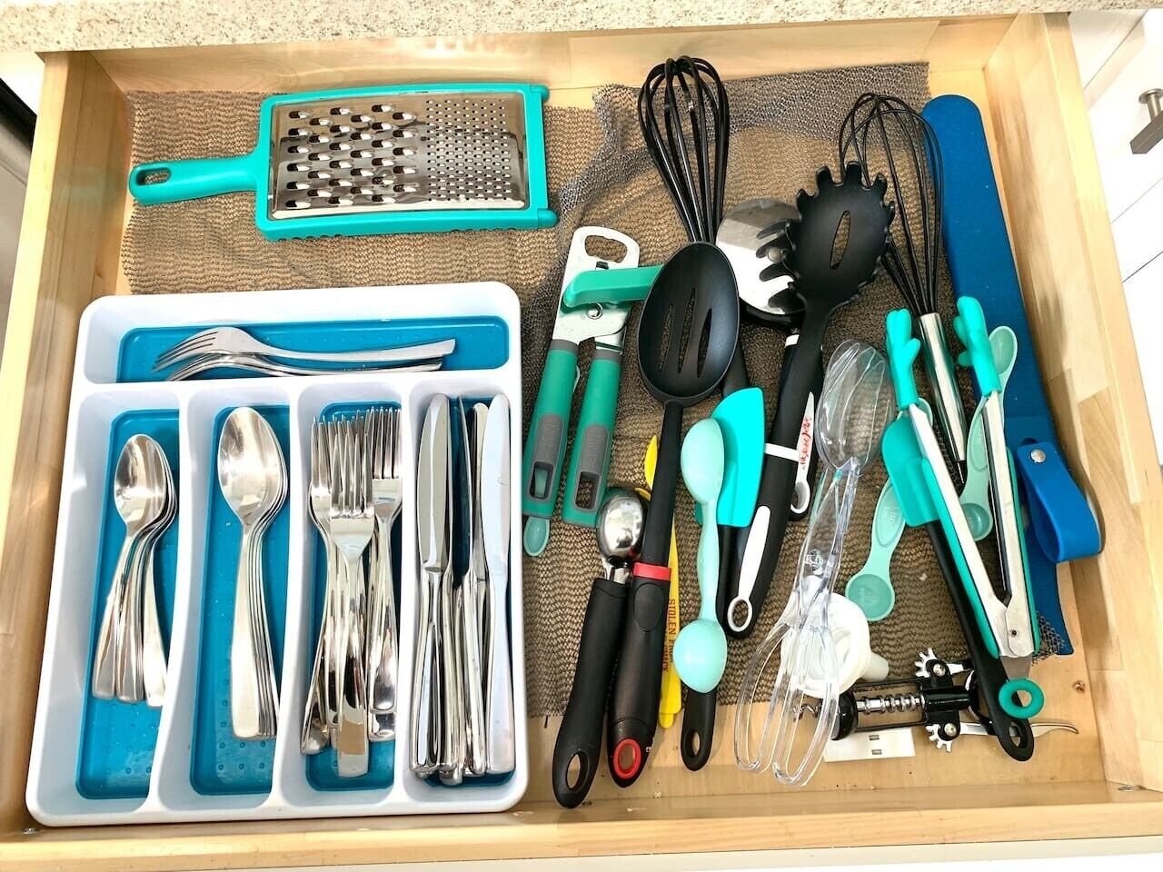 A drawer with kitchen utensils and tools, including a grater, spatula, whisk, and various cutting tools.